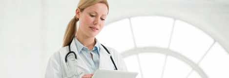 Image of a female Doctor-in-white-coat with- stethoscope typing on an ipad